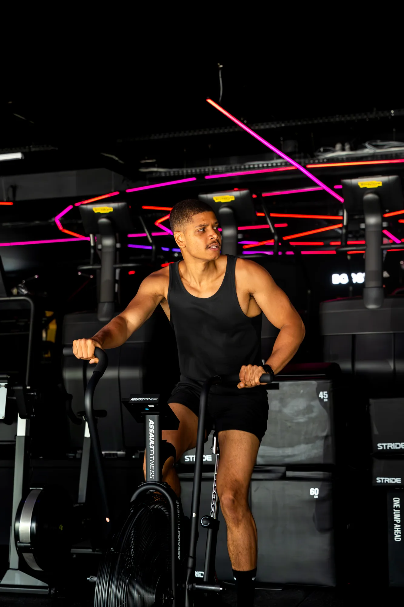 Member on the assault bike under coloured neon at ONE PULS Brussels