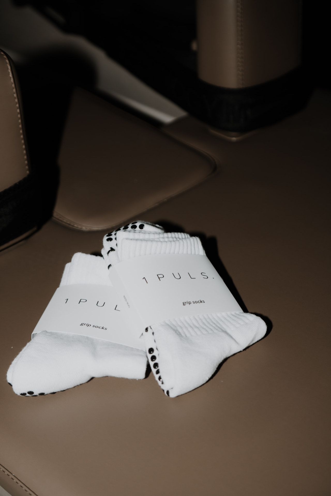1PULS. branded white grip socks resting on a leather bench at ONE PULS Brussels