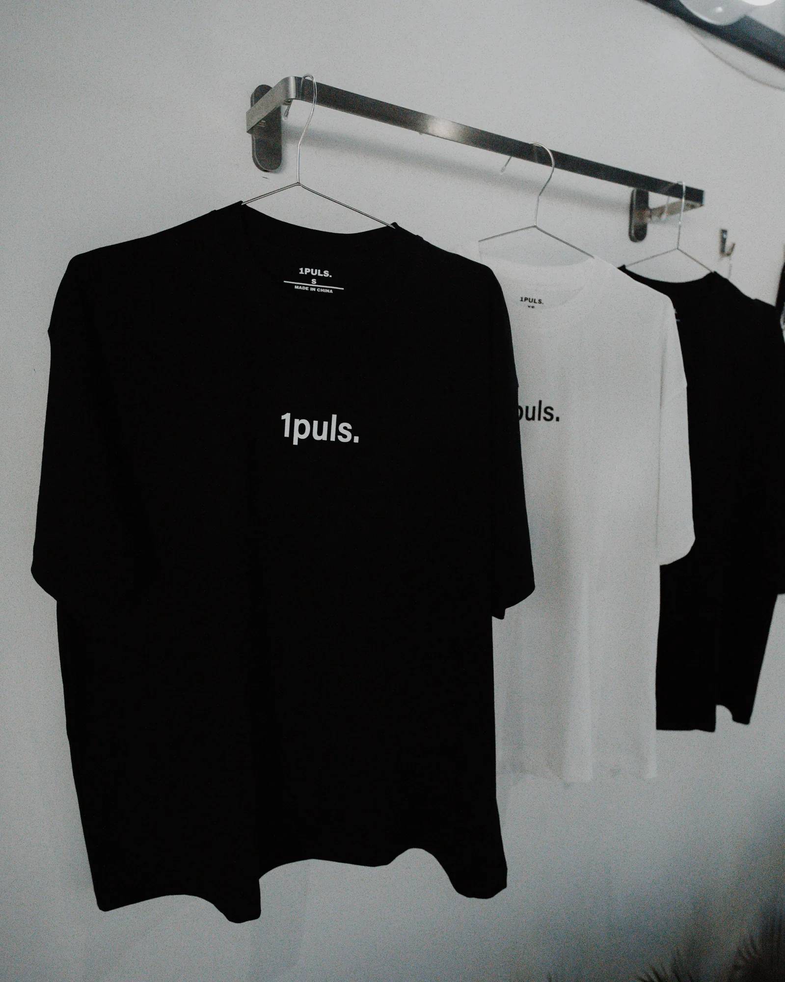 1PULS. club t-shirts hanging on a rail at ONE PULS Brussels