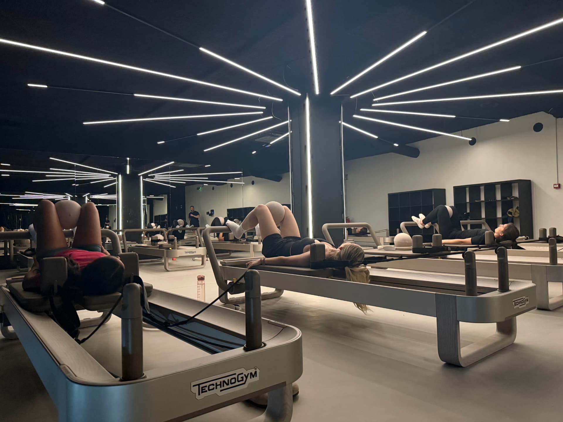 Technogym reformer Pilates class under linear neon lighting at ONE PULS Brussels