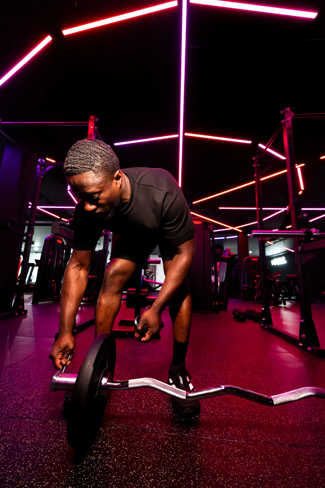 Member loading an EZ bar under neon lighting in the ONE PULS open gym, Brussels