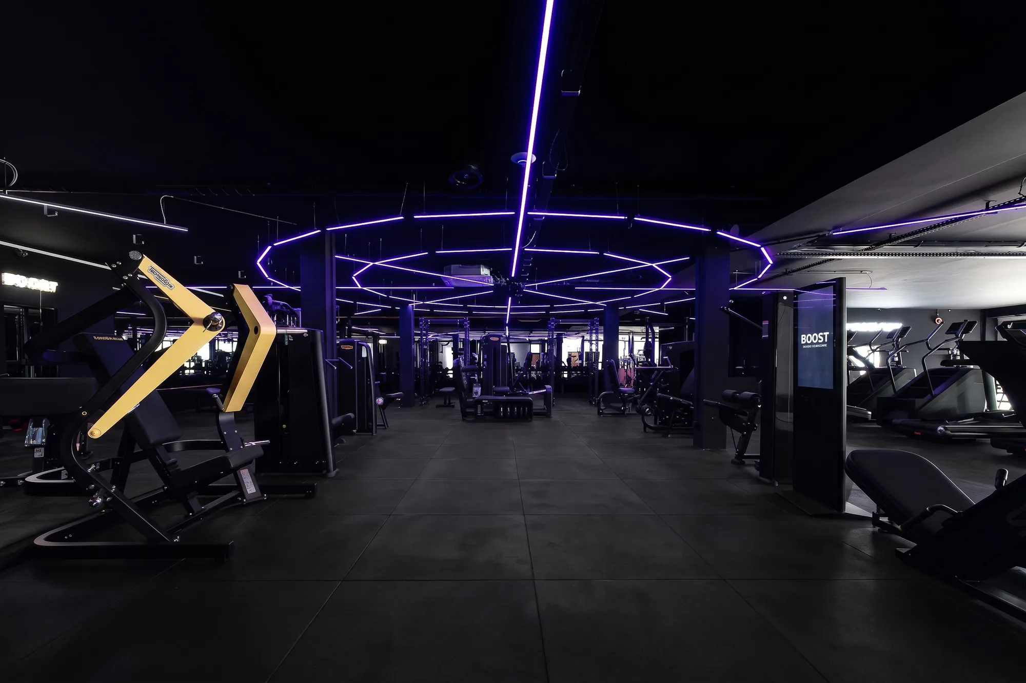 Open Space training floor with strength machines and violet neon lighting at ONE PULS Brussels